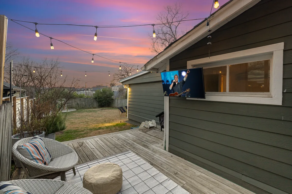 This exterior backyard scene shows string lights, an outdoor seating area, and a television screen, evoking a cozy, festive atmosphere. It suggests settings for outdoor movie nights, s’mores, and relaxed gatherings under the stars.