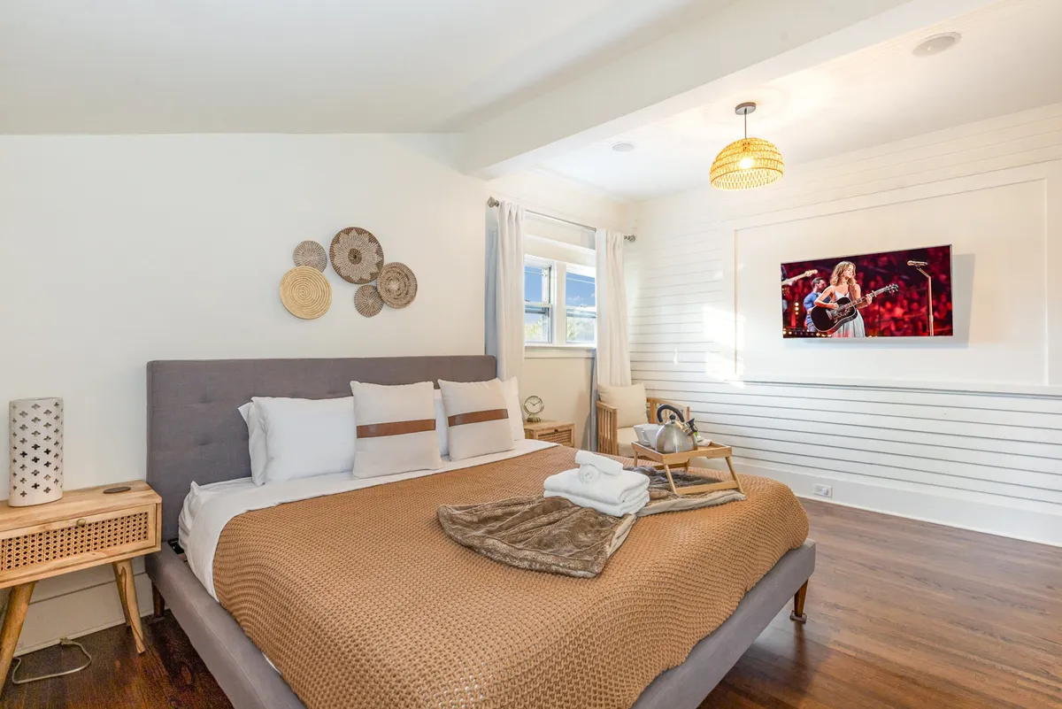 A warm bedroom featuring a bed with brown and white bedding, decorative wall plates, and a television framed with a performance image. The mood feels welcoming and restful, offering privacy and comfort.