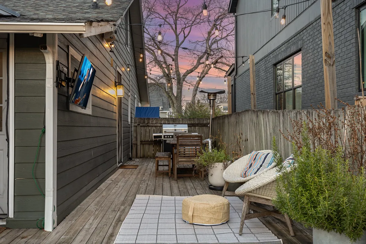 A stylish and comfortable outdoor seating area at The Retreat, featuring a wall-mounted TV, string lights, a grill, decorative plants, and relaxed seating. The evening ambiance is perfect for group gatherings, outdoor dining, or unwinding under the stars after a night out.