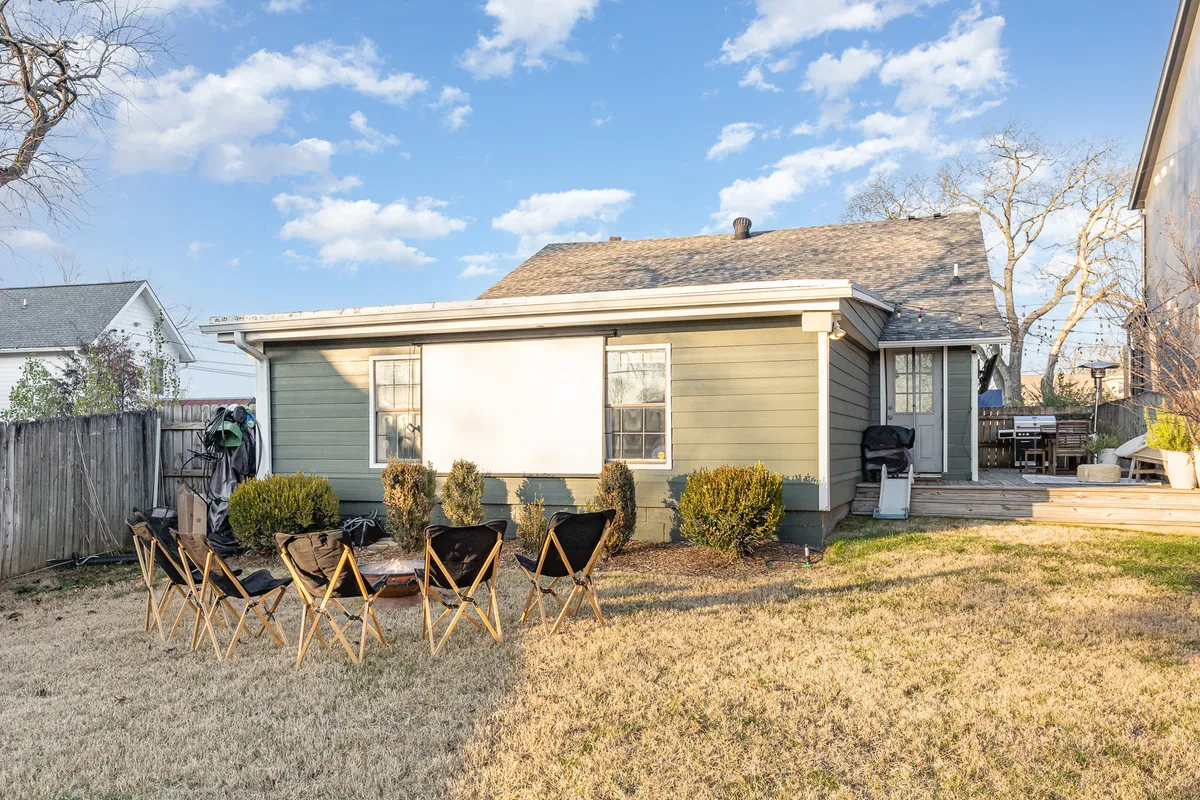 A backyard seating and patio area with green exterior house walls, outdoor furniture, and ample space for gatherings. The scene evokes relaxed, casual family time outdoors.