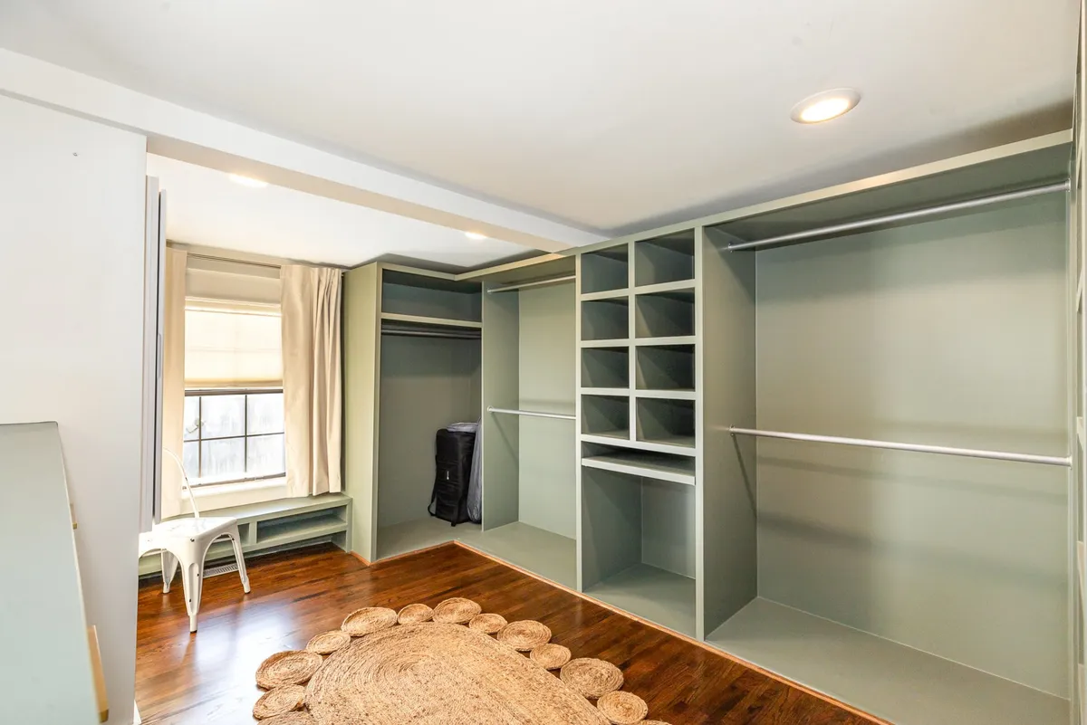 An organized open closet space illuminated by gentle natural light from a window, with a decorative rug on the floor. The closet is spacious and inviting, perfect for storing clothing and belongings during longer stays.