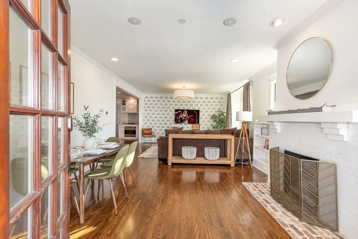 A spacious, inviting living and dining area with a central dining table surrounded by comfortable chairs, a cozy sofa, a fireplace, and tasteful wall art. The space is perfect for family meals, gatherings, and relaxing together.