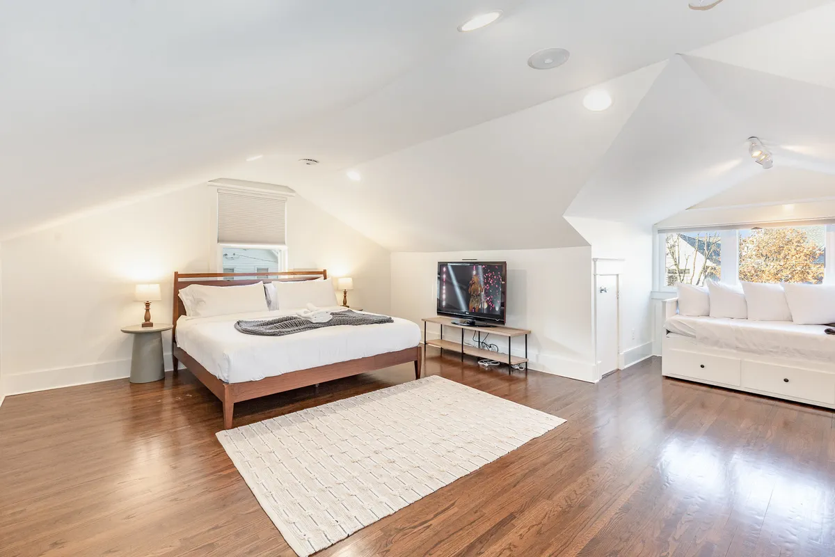 A tranquil bedroom featuring a king-sized bed adorned with plush linens, large windows letting in natural light, a comfortable seating area, and a wall-mounted TV. The space feels cozy and inviting, perfect for relaxing after exploring the city.