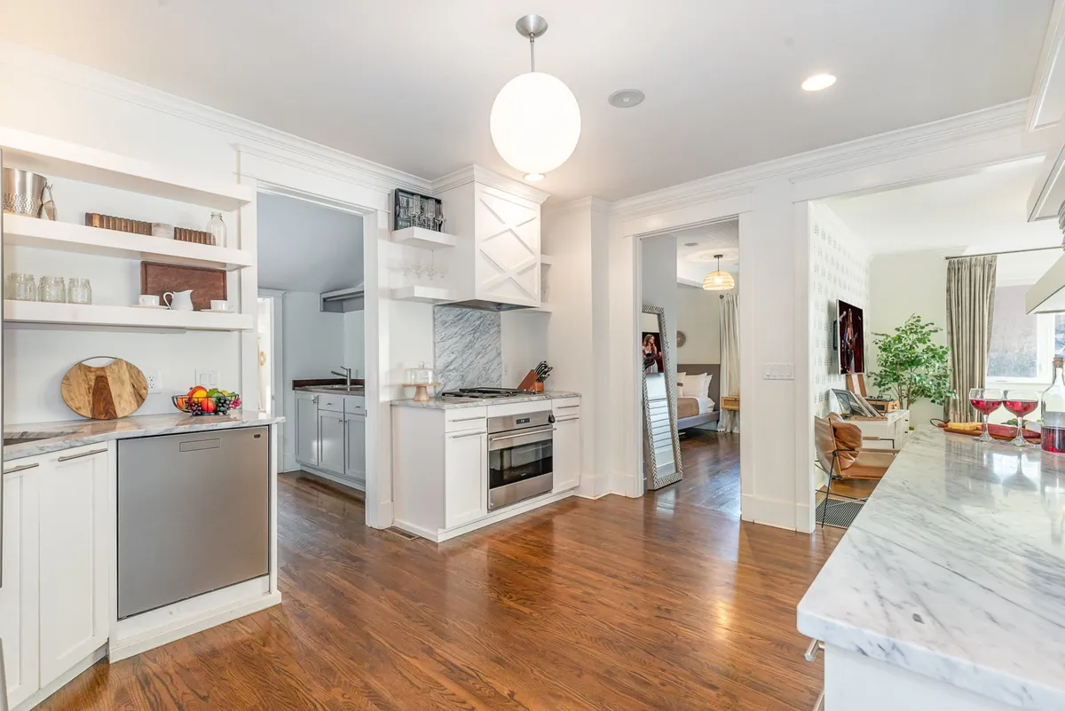 A modern kitchen with sleek appliances, marble countertops, open shelving, and wooden flooring. The layout is bright and functional, ideal for preparing meals and gathering with loved ones.
