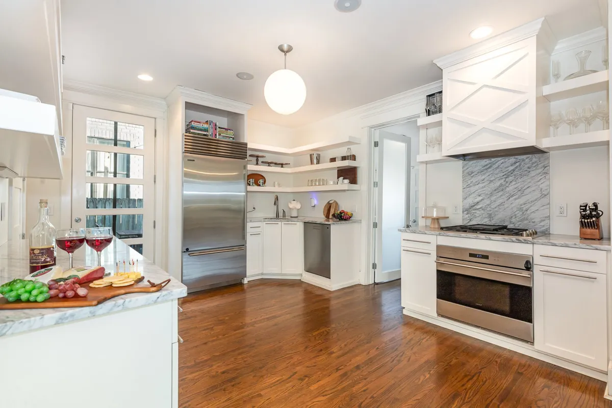 A modern, chef-ready kitchen with a marble countertop, stainless steel appliances, open shelving with glassware, and a welcoming fruit platter. The kitchen is spacious and designed for both cooking and entertaining, offering everything needed for group meal preparation and shared culinary experiences.