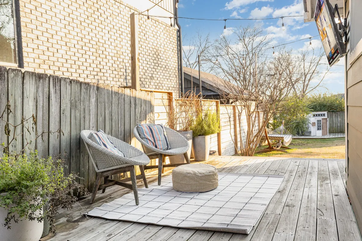A cozy outdoor setup featuring two lounge chairs, a round pouf, and decorative plants in a private, fenced yard. The space is ideal for relaxing, reading, or enjoying an outdoor meal, surrounded by a sense of comfort and security.